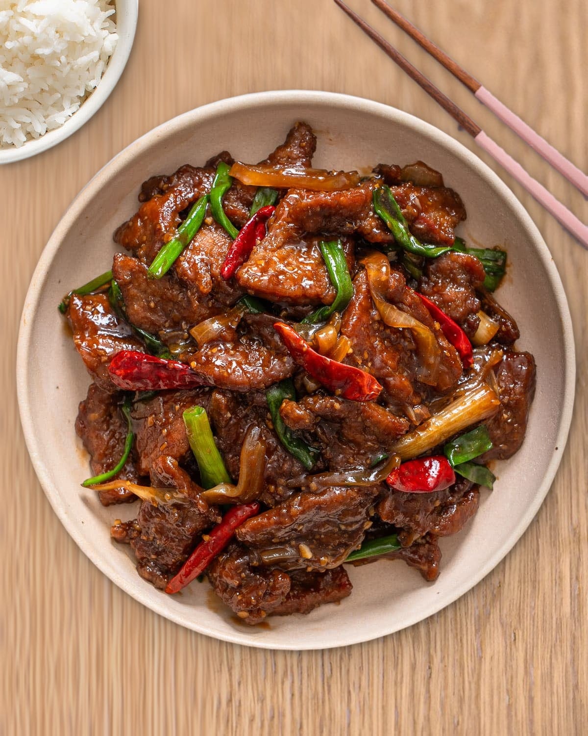 Bò xào dầu hào — beef stir-fried in oyster sauce with spring onion and dried chilli, with steamed rice and chopsticks on a wooden table