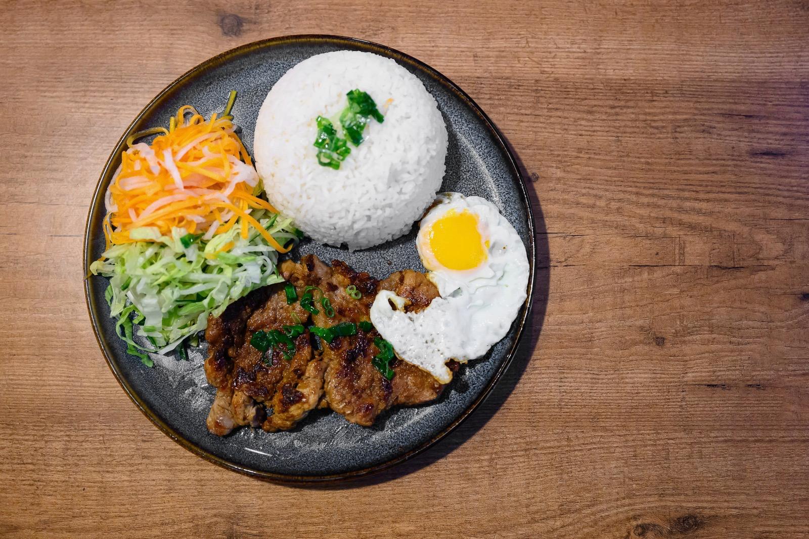 Cơm tấm — grilled pork rib with broken rice, a fried egg, cucumber, tomato and fish sauce