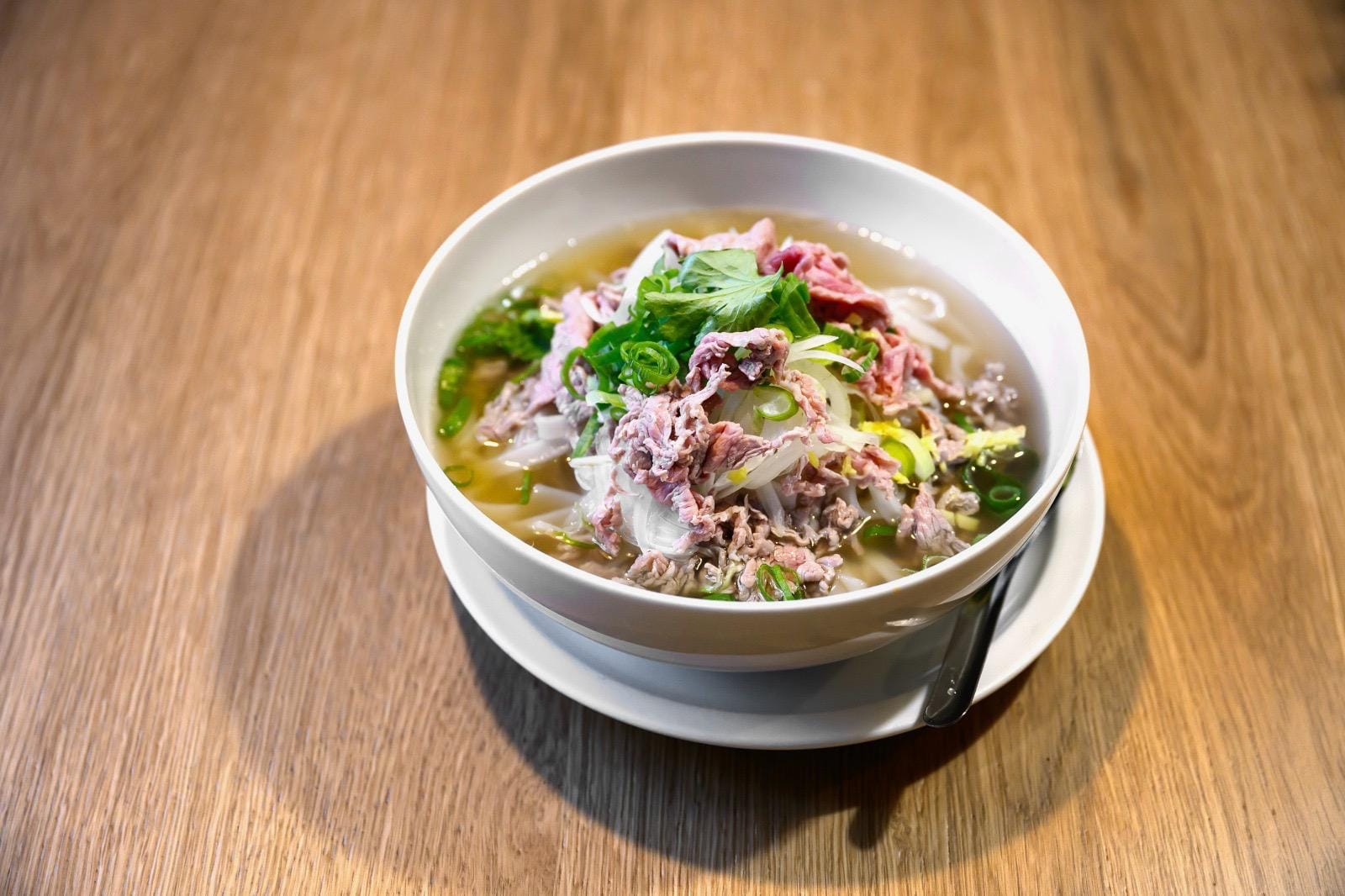 Bowl of pho with sliced beef, spring onion and rice noodles